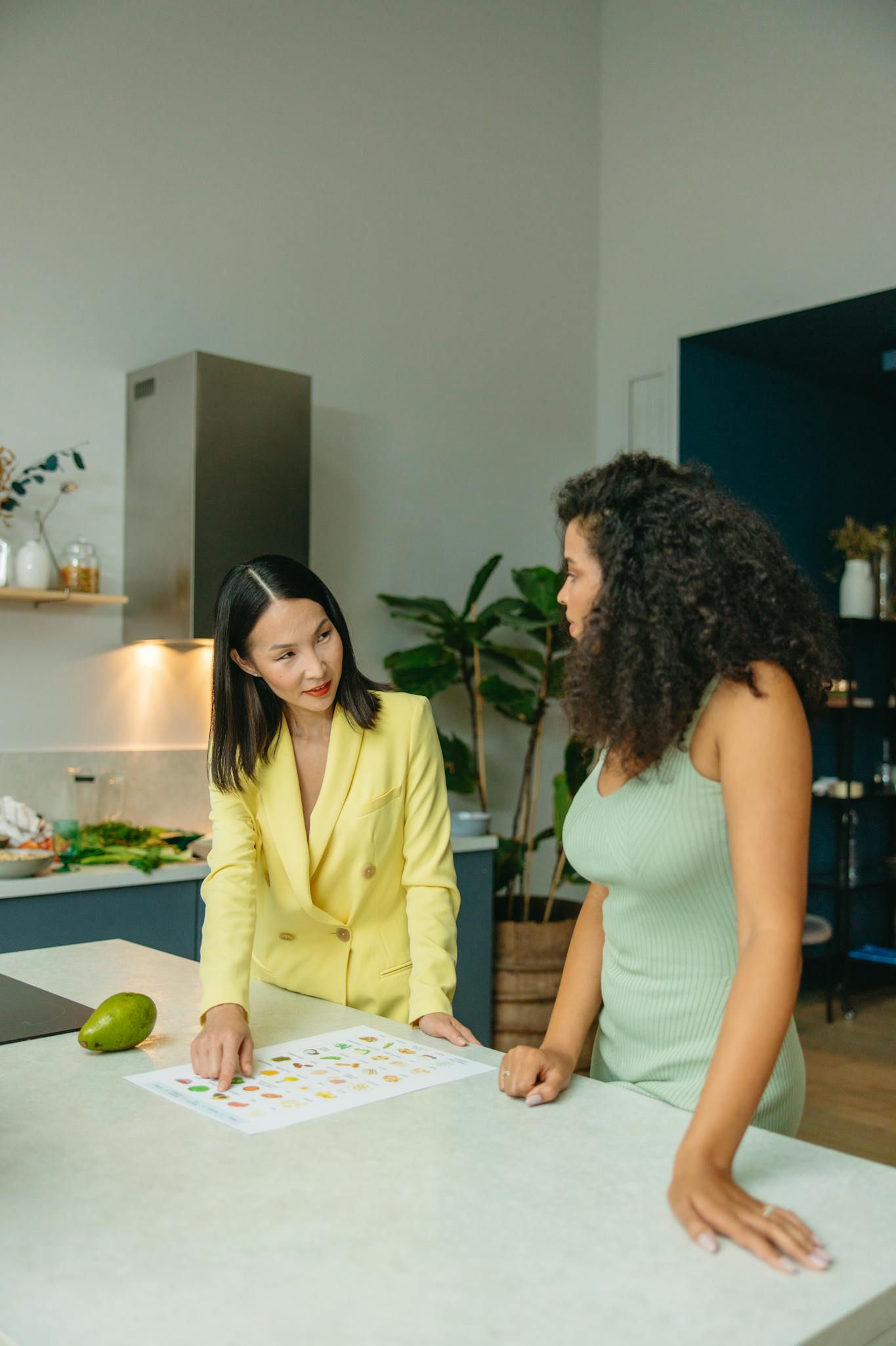 Two women discussing healthy eating in a stylish kitchen setting with fresh vegetables.